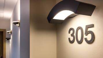 A hallway with a number '305' illuminated on the wall, a door, and a light fixture.