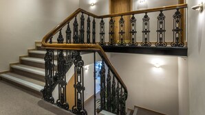 Una escalera con barandales negros ornamentados y un pasamanos de madera, que conduce a un piso superior.