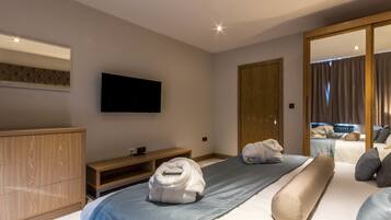 A modern hotel room with a large bed, a wooden wardrobe, a flat-screen TV, and a mirror.