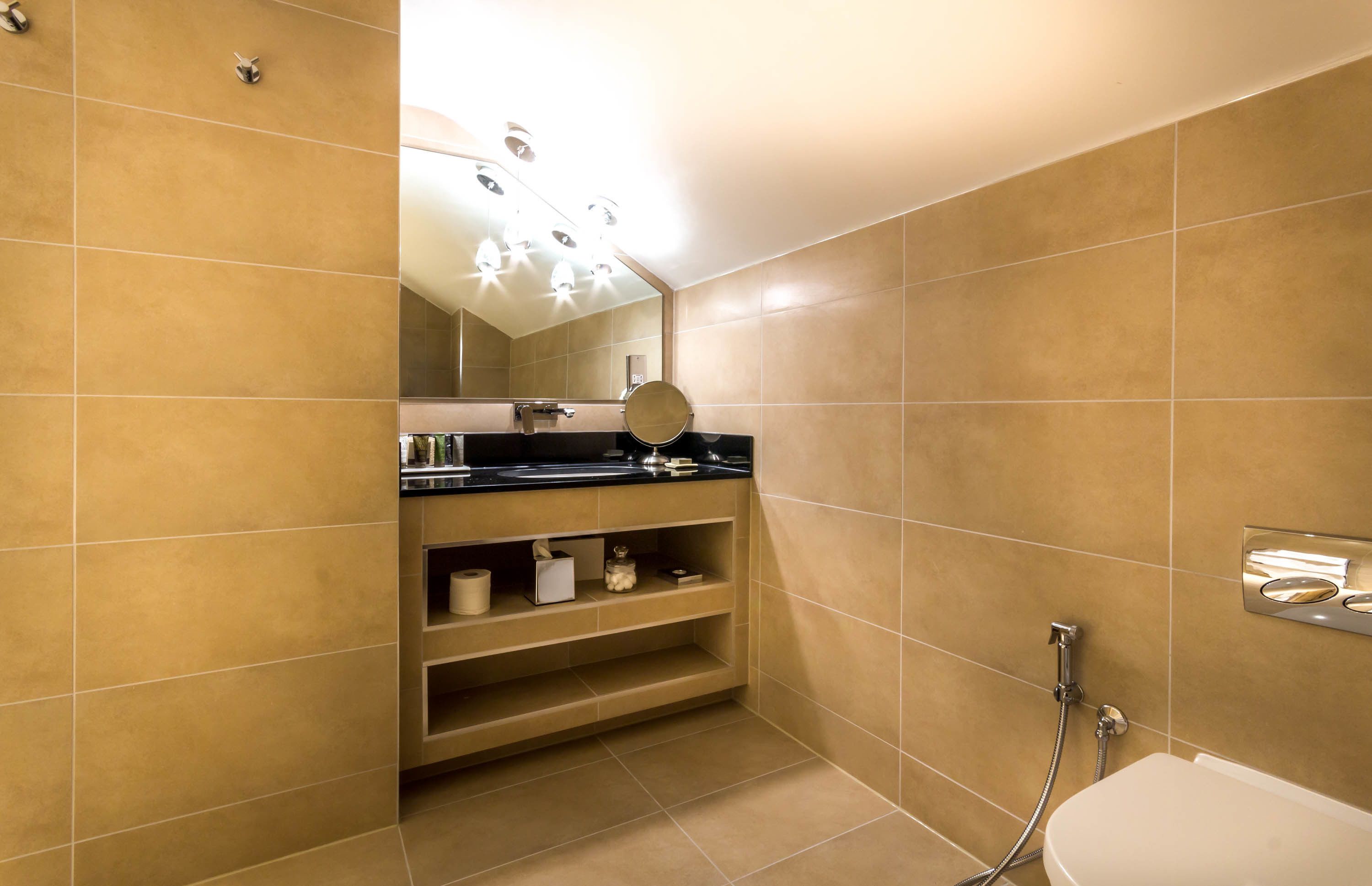 A modern bathroom with beige tiles, a black countertop, a mirror, a toilet, and a shower.