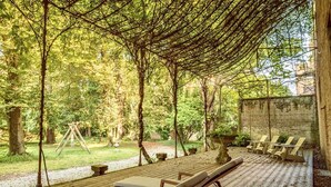An outdoor seating area with wooden benches and a swing set, surrounded by trees and a brick wall. - Palazzo Mantua Benavides Suites and Apartments (Padova)