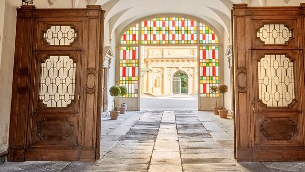 A grand entrance with two wooden doors featuring intricate designs, leading to a brightly lit interior with a colorful stained glass window. - Palazzo Mantua Benavides Suites and Apartments (Padova)