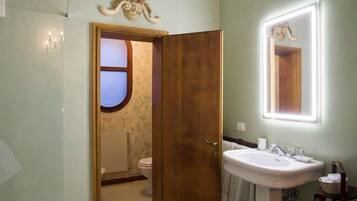 A bathroom with a wooden door, a white sink, and a mirror with a lighted frame.