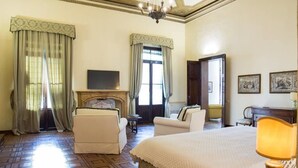 A hotel room with a large bed, two armchairs, a television, and a fireplace. - Palazzo Mantua Benavides Suites and Apartments (Padova)