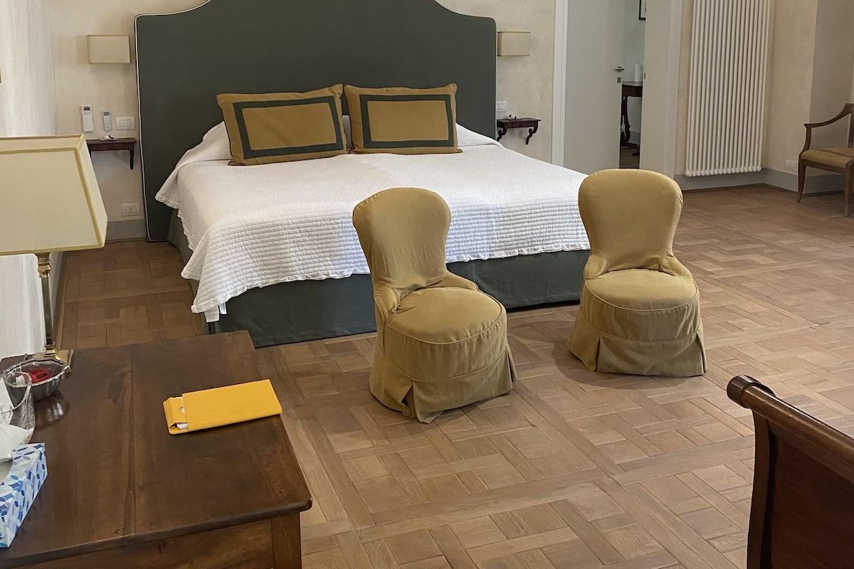 Un dormitorio con una cama grande, dos sillones, una mesa de madera y una mesita de noche con lámpara.