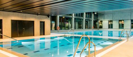 An indoor swimming pool with clear water, metal railings, and a modern ceiling design.