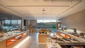 Un desayuno buffet moderno con diferentes opciones de comida y una vista de un edificio al fondo.