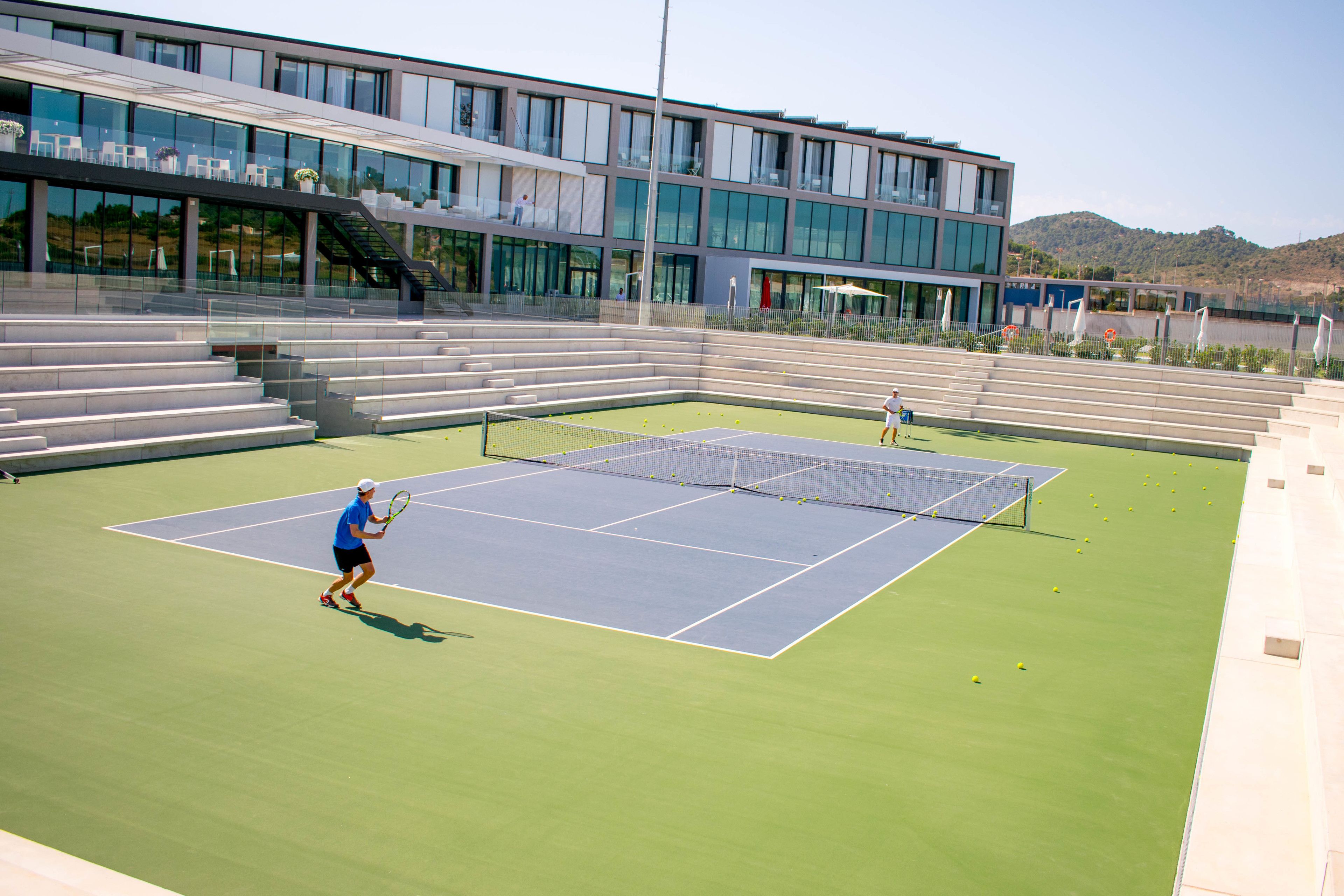 Un court de tennis avec des gradins et un bâtiment moderne en arrière-plan.