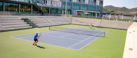 A tennis court with bleachers and a modern building in the background.