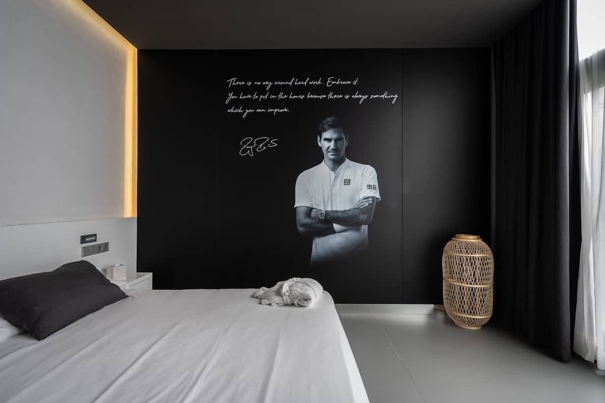 A modern bedroom with a large bed, a bedside table, a wall-mounted light, and a decorative wall piece.