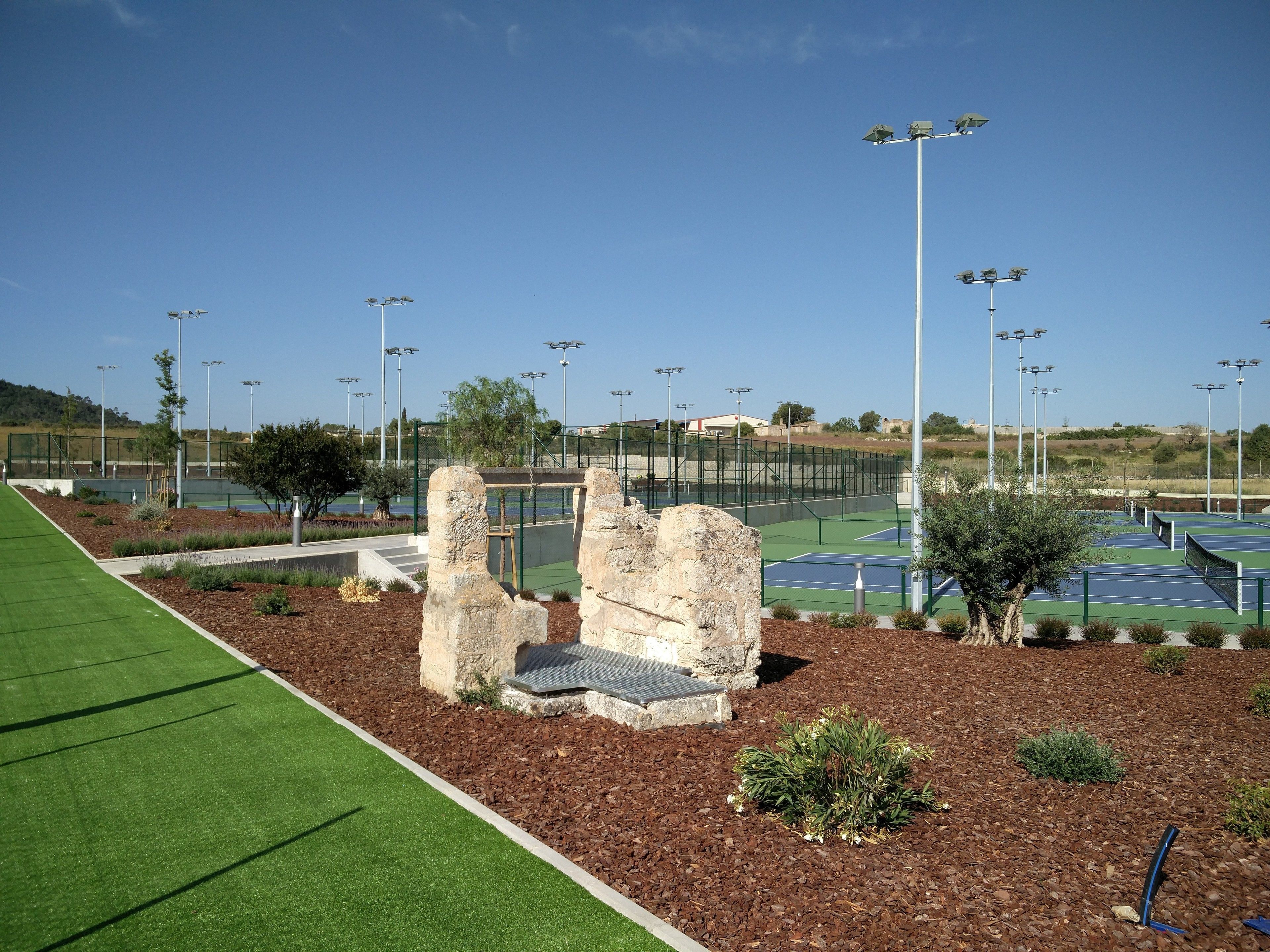 Una cancha de tenis con jardines y estructuras de piedra.