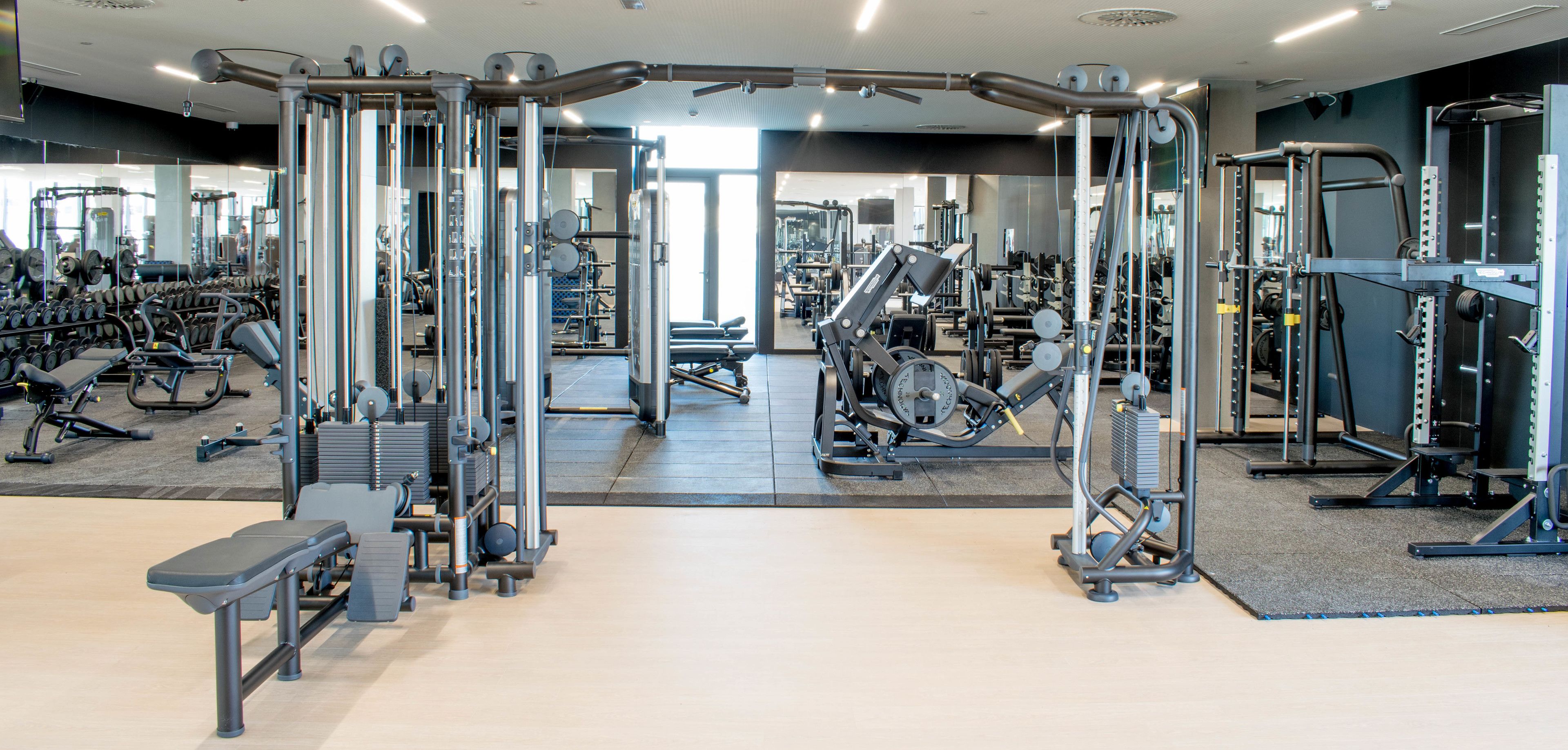 A gym with various exercise machines and weights, a bench, and a mirrored wall.