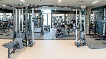 A gym with various exercise machines and weights, a bench, and a mirrored wall.