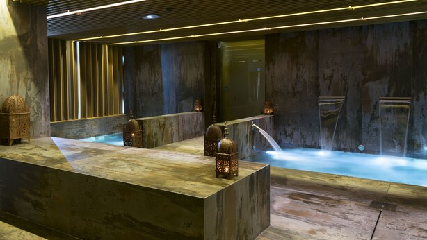 Un espacio moderno de spa con un mostrador de recepción de piedra, un espejo grande y una fuente de agua.