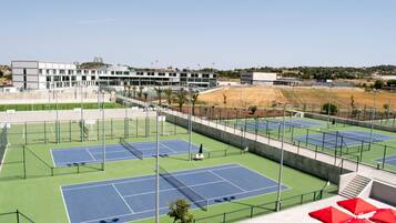 Un complexe de courts de tennis comprenant plusieurs terrains, un bâtiment en arrière-plan et des parasols rouges.