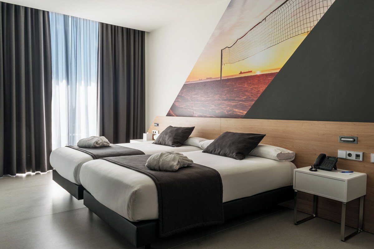 Une chambre d’hôtel moderne avec un grand lit, une table de chevet avec un téléphone et un téléviseur fixé au mur.