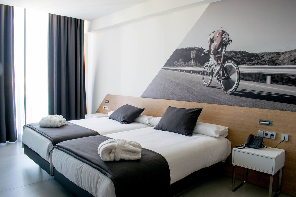 A hotel room with two beds, a nightstand, and a large wall mural of a cyclist.