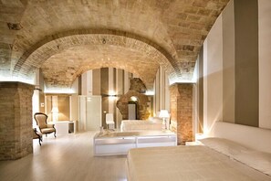 A hotel room with a stone archway, a bed, a sofa, and a chair. - Hotel degli Affreschi (Montefalco)