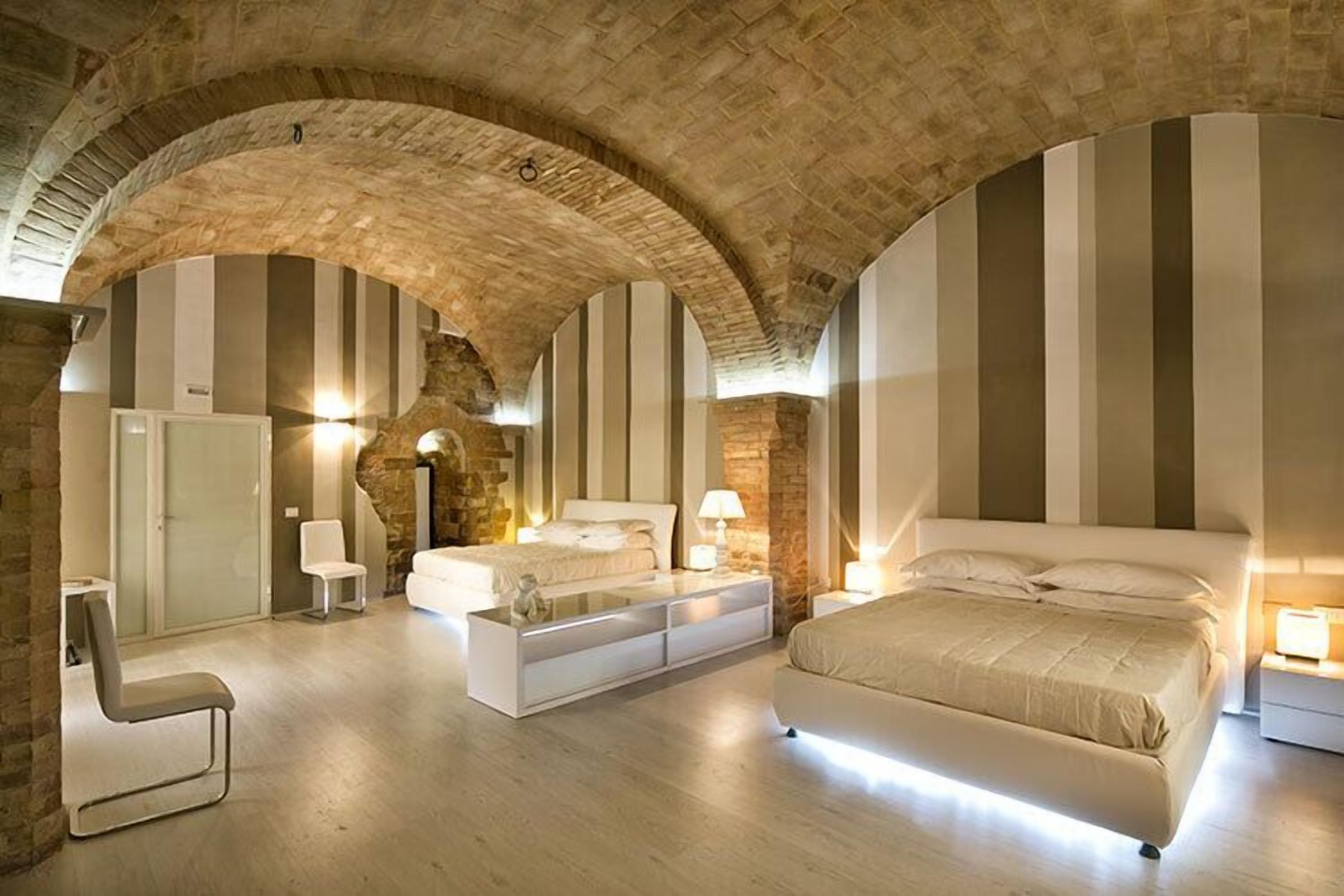 Un dormitorio moderno con techo abovedado de piedra, una cama grande, mesitas de noche y una zona de estar.