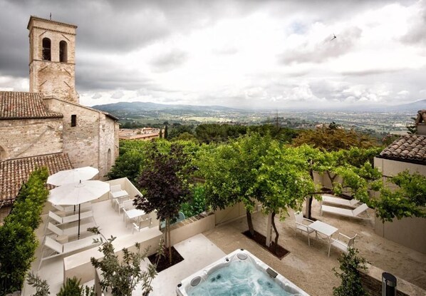 Terraza en la azotea con mobiliario exterior, jacuzzi y vistas a un edificio histórico y al paisaje.