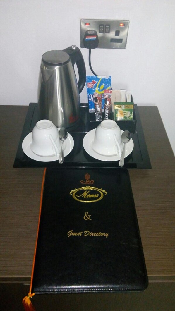 Disposição para o café da manhã em um quarto de hotel, com uma cafeteira, duas xícaras, um tabuleiro com sachês de café e chá, e um menu e guia do hóspede sobre a mesa.