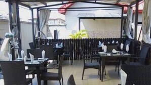 Un restaurante al aire libre con mesas y sillas, piso de baldosas y una zona cubierta con vista a la calle.