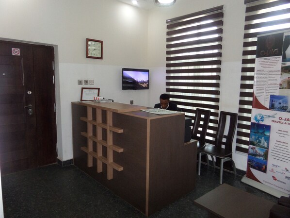 A reception desk with a clock, a television, and a bulletin board in a hotel lobby. - O-jays Guest House (Abuja)