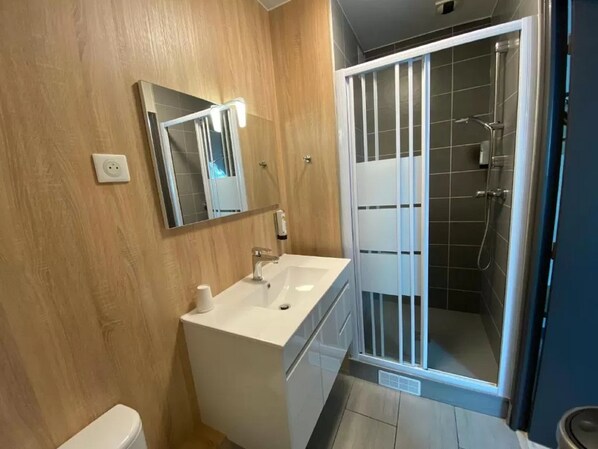 Un baño con pared de madera, un lavamanos blanco, un espejo, cabina de ducha y un inodoro.