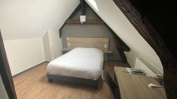 Et lille, trekantet soveværelse på loftet med seng, skrivebord og stol.