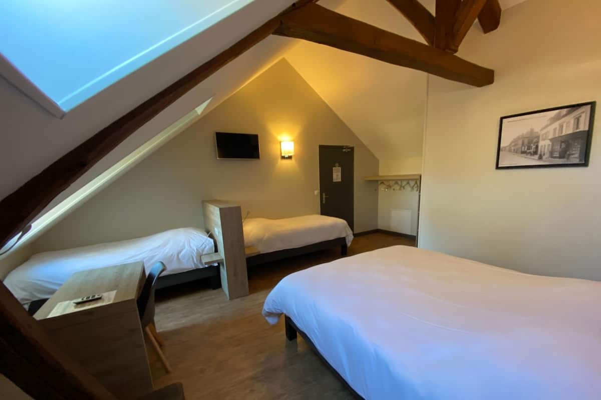 A dormitory-style room with two single beds, a wooden bench, a wall-mounted TV, and a door with a coat rack.
