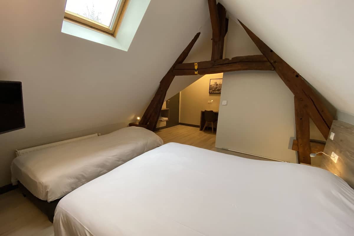 A bedroom with two beds, a skylight, wooden beams, a desk, and a chair.