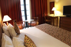 A hotel room with a bed, two chairs, a desk, a television, and two lamps. - Hôtel Le Consul (Tunis)