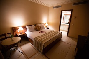 Une chambre d’hôtel avec un lit, des tables de chevet, une petite table ornée d’un vase de fleurs et donnant sur la salle de bain.