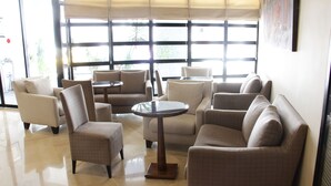 A hotel lobby with a seating area featuring sofas and armchairs, a round table, and large windows with blinds. - Hôtel Le Consul (Tunis)