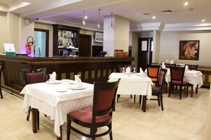 Un restaurante con varias mesas y sillas, una zona de bar y un reloj en la pared.