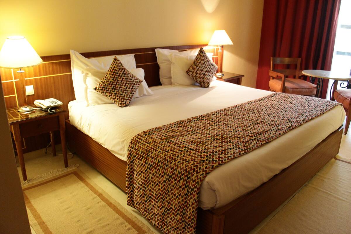 A hotel room with a large bed, two bedside tables with lamps, a small table, and a chair.