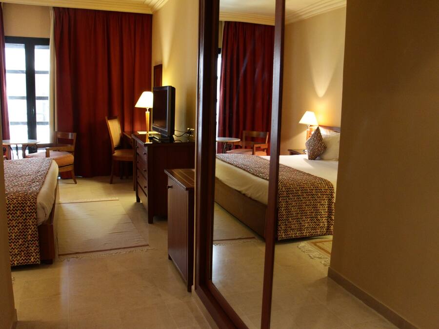 A hotel room with two beds, a desk, a chair, a television, and a lamp.