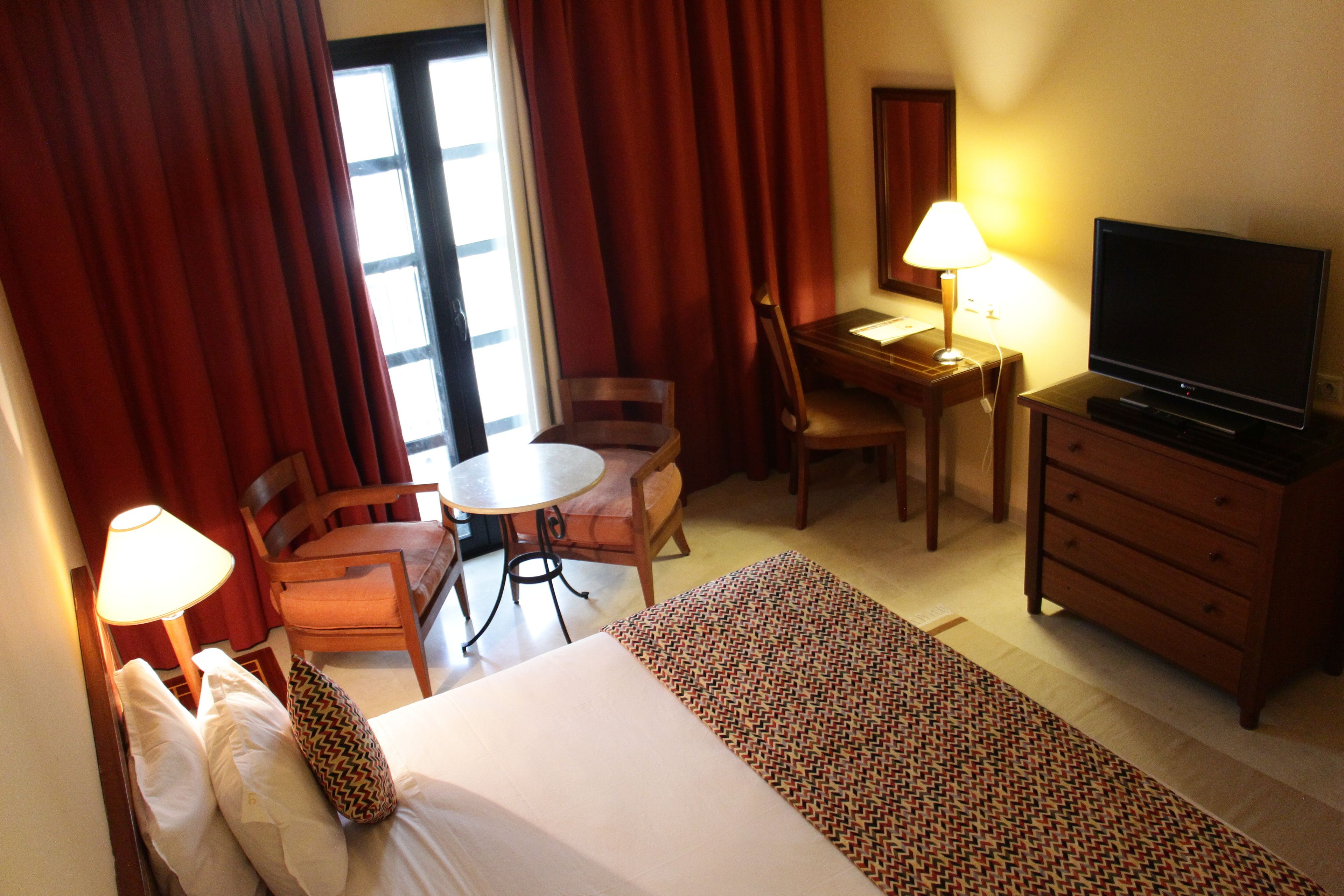A hotel room with a bed, a desk, a chair, a television, and a lamp.