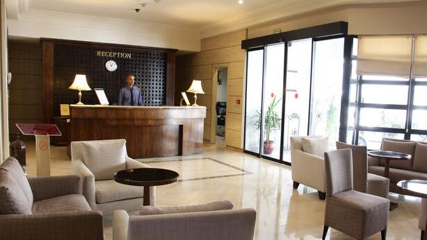 A reception area with a wooden reception desk, a clock, and a receptionist. There are several seating areas with chairs and tables. - Hôtel Le Consul (Tunis)