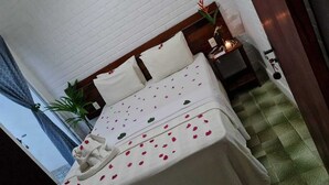 A neatly made bed with a white bedspread adorned with pink and green floral patterns, a wooden headboard, and a small bedside table with a lamp. - Pousada Vila Anaua (Japaratinga)