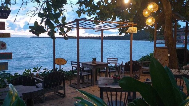 An outdoor seating area with tables and chairs, surrounded by greenery, overlooking a body of water. - Pousada Vila Anaua (Japaratinga)