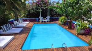 A rectangular swimming pool with a wooden deck, surrounded by lounge chairs and potted plants. - Pousada Vila Anaua (Japaratinga)