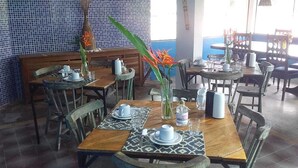 A restaurant with wooden tables and chairs, some with placemats. There are vases with flowers on the tables. - Pousada Vila Anaua (Japaratinga)