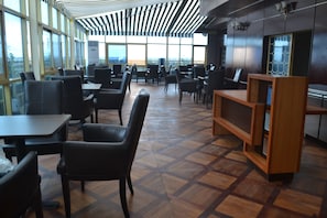 A spacious indoor area with multiple tables and chairs, large windows, and a patterned wooden floor. - Noubou International Hotel (Douala)