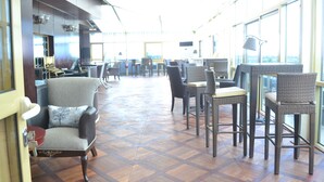 A spacious indoor area with multiple seating arrangements, including chairs and tables, and large windows providing natural light. - Noubou International Hotel (Douala)