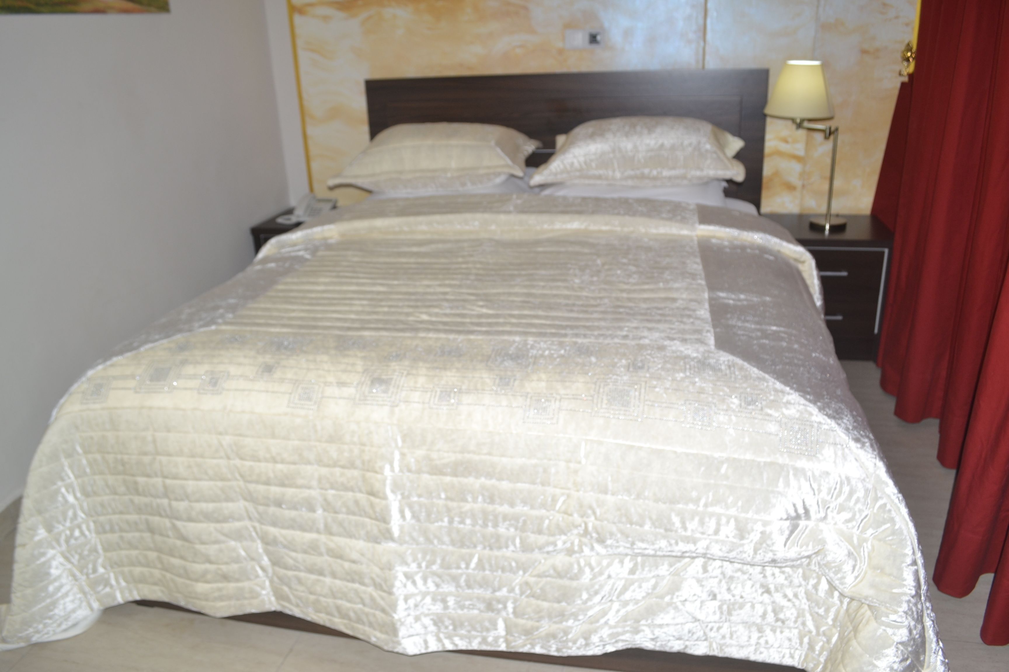 Cama bem arrumada com cobre acolchoado, luminária de cabeceira e mesa de cabeceira com abajur.