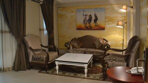A living room with a sofa, armchairs, a coffee table, and a painting on the wall. - Noubou International Hotel (Douala)