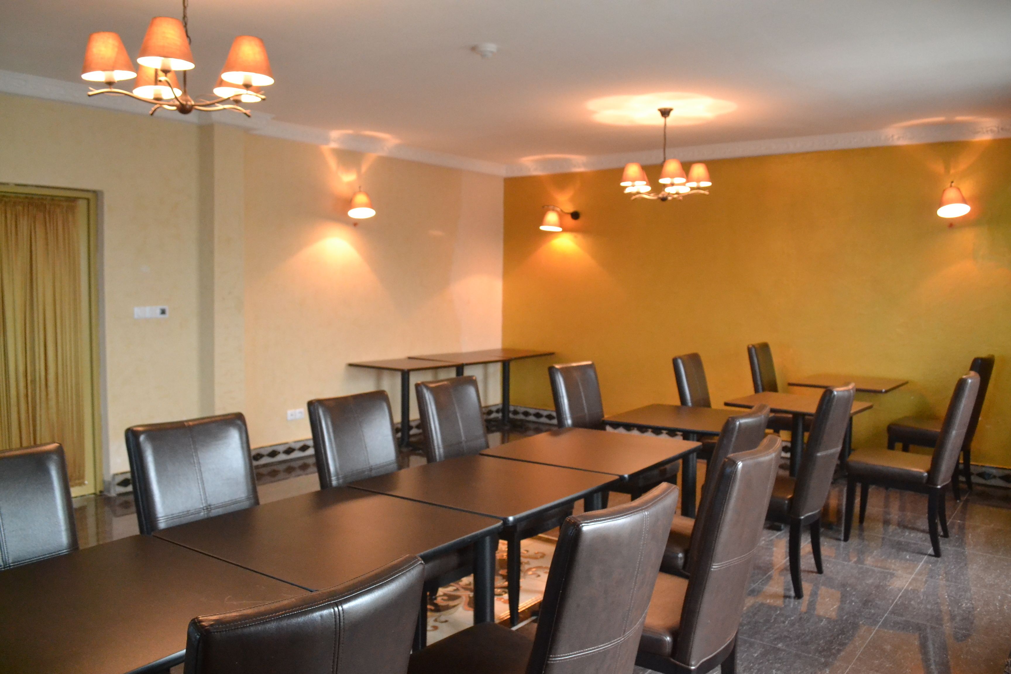 A conference room with a long table and multiple chairs, equipped with a chandelier and wall-mounted lamps.