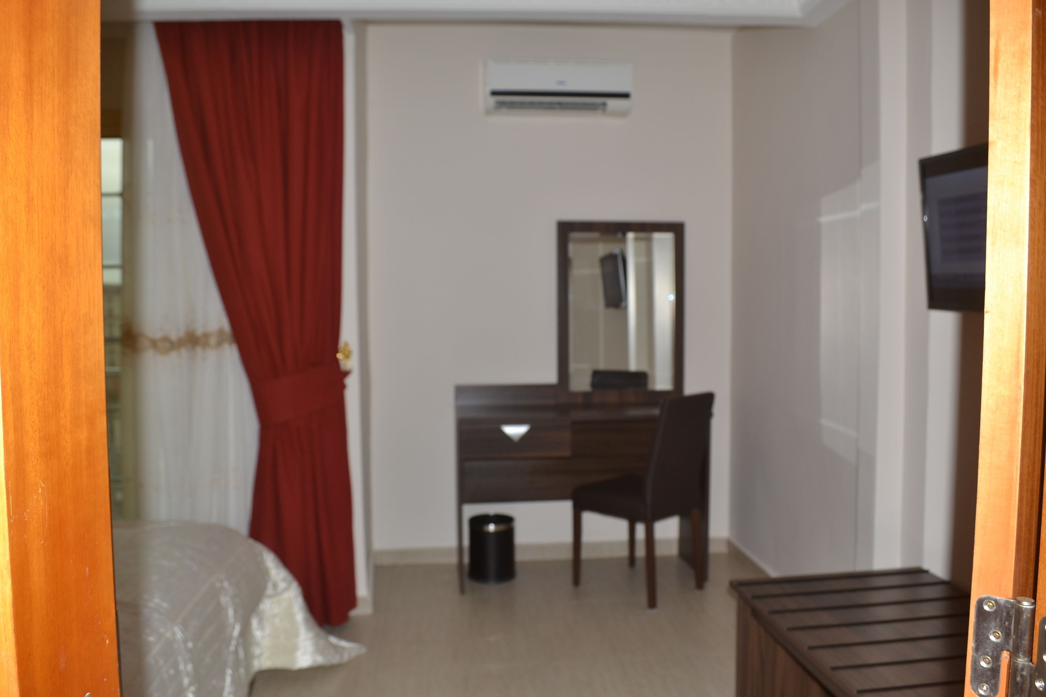 A hotel room with a bed, a desk with a chair, a mirror, an air conditioning unit, and a television on the wall.