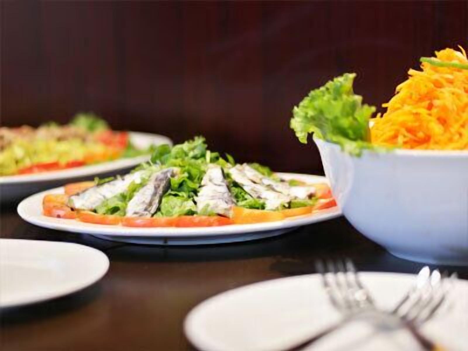 Een eettafel met borden eten, waaronder een salade met sla en geraspte wortelen, en een schaal met geraspte wortelen.